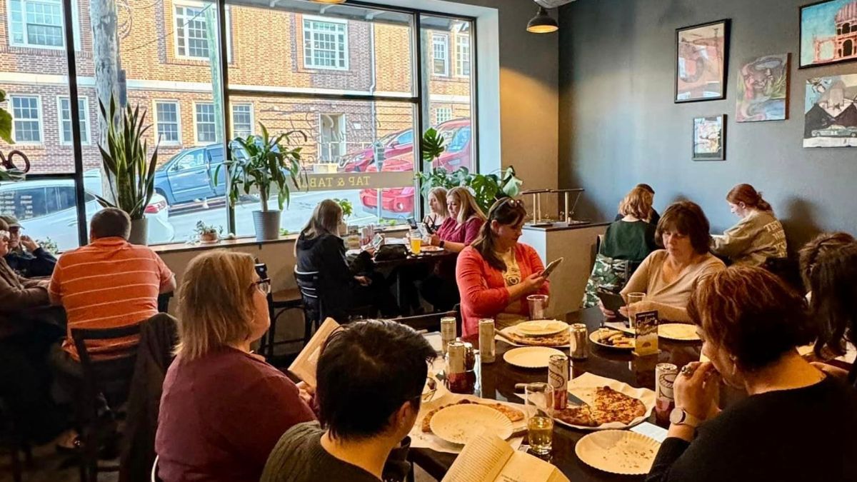 A group of people gathered around several tables, all quietly reading at Silent Book Club Westmoreland County