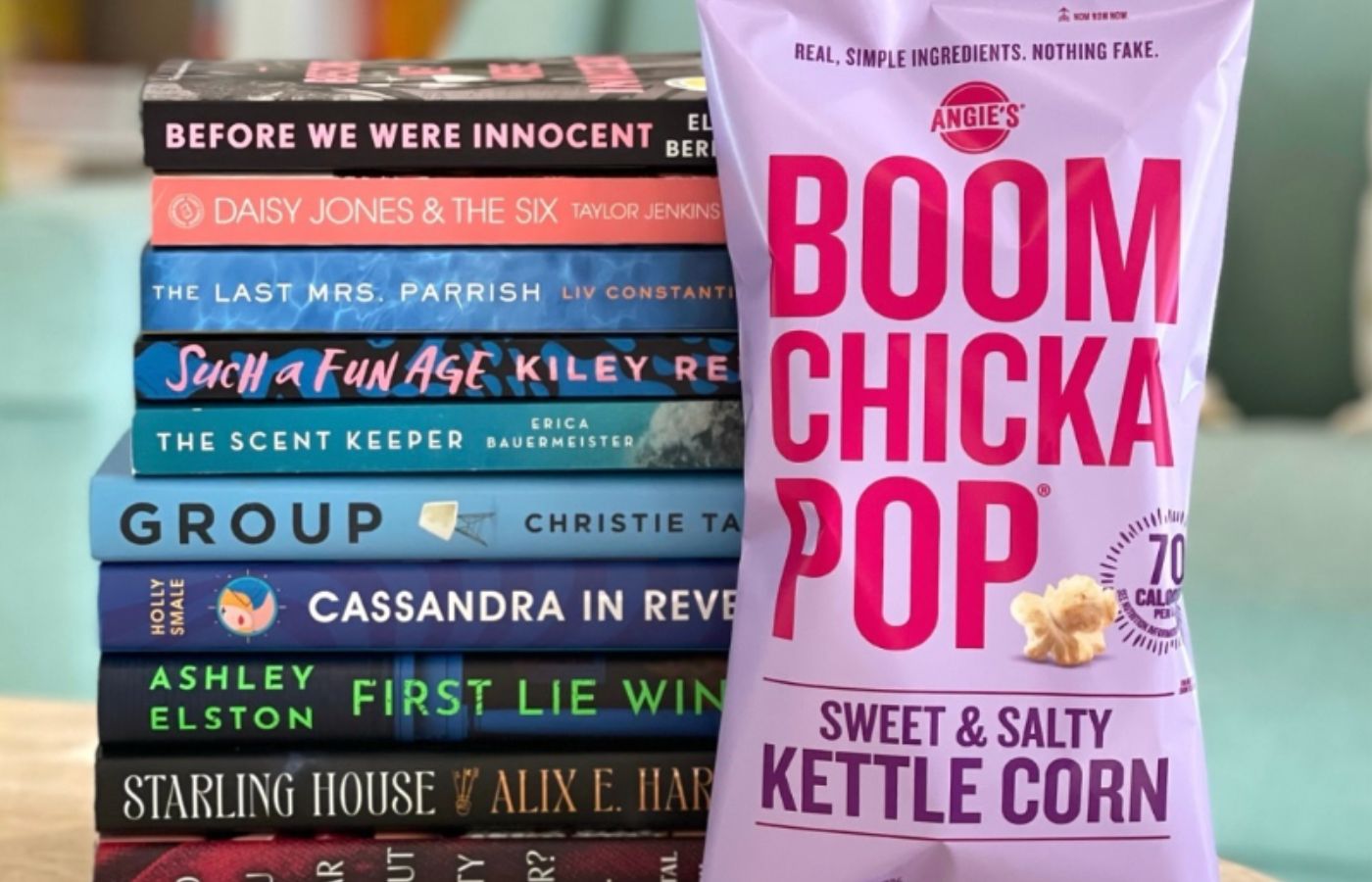 A stack of book picks from Reese's Book Club and a bag of Boom Chicka Pop opcorn