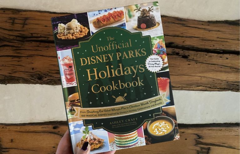 The Unofficial Disney Parks Holidays Cookbook cover, held up in front of a log cabin wall